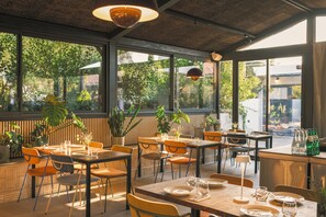 An indoor dining area with tables and chairs, large windows, and potted plants. - Gandum Village - Conscious Boutique Hotel (Montemor-o-Novo)