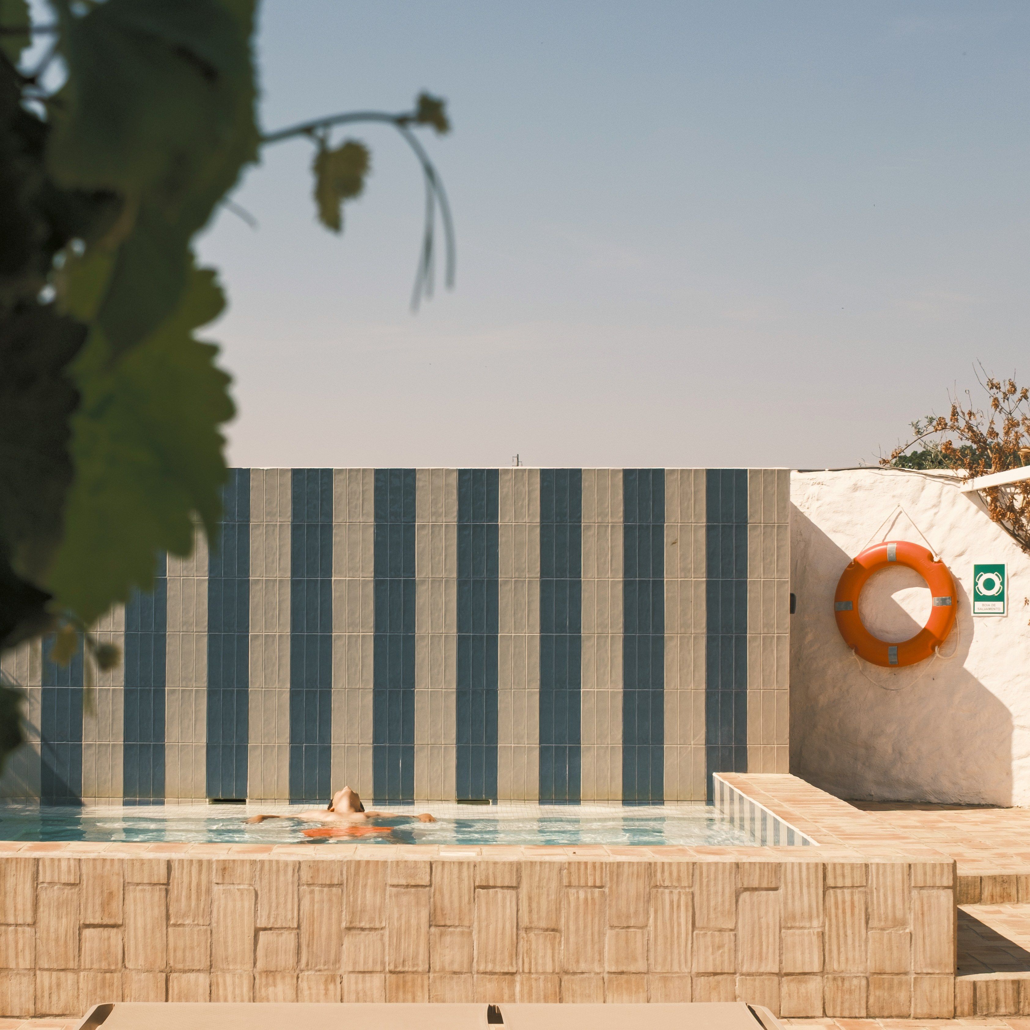 A swimming pool with a person in the water, a lifebuoy, and a sign indicating a lifeguard on duty.