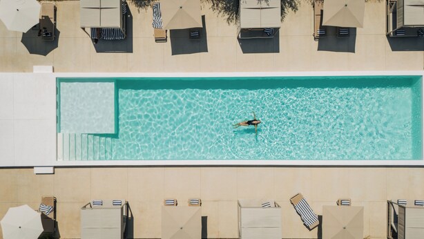 Une piscine rectangulaire à l’eau claire, entourée de chaises longues et de parasols.