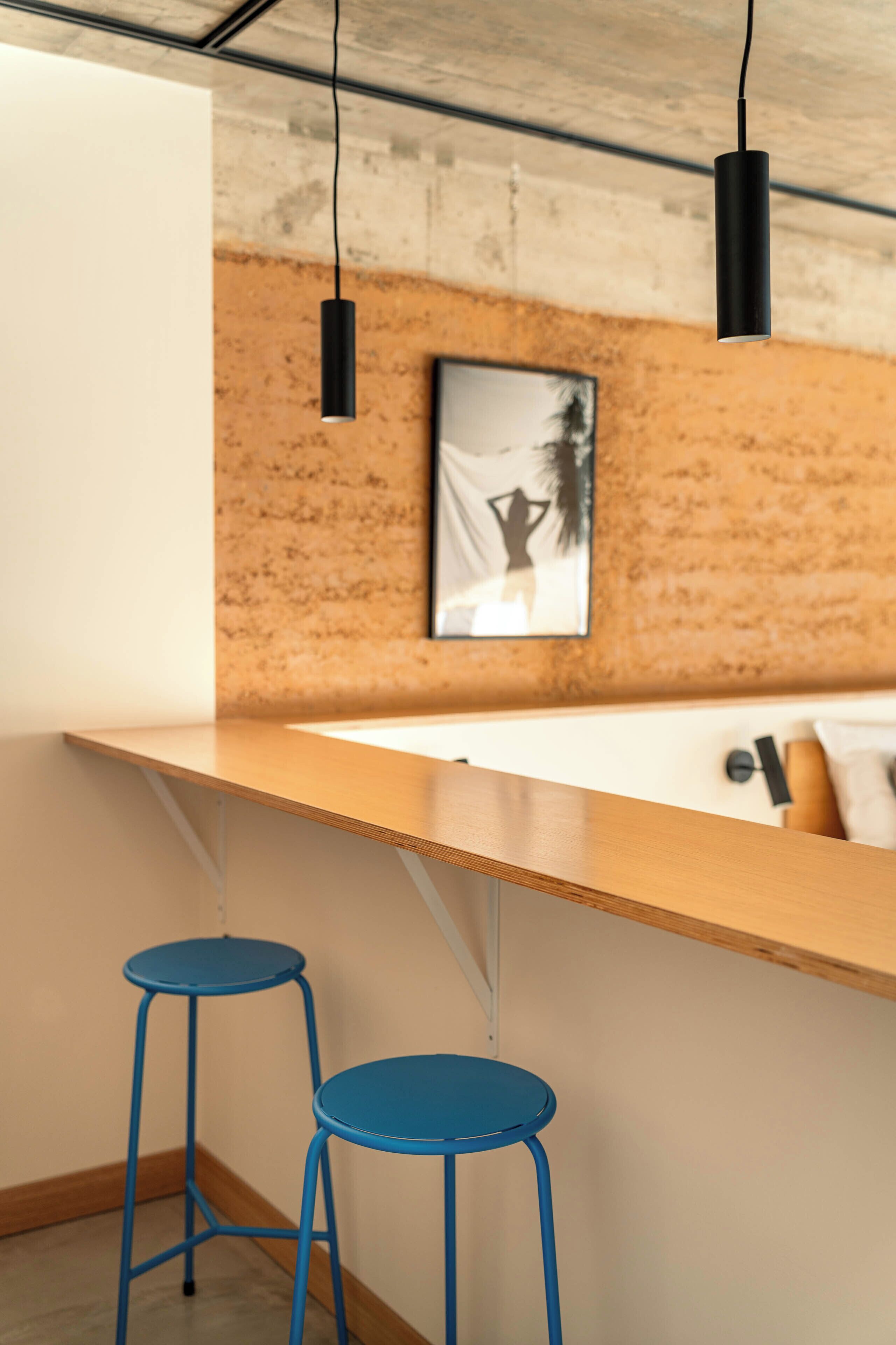 Una cocina moderna con encimera de madera, dos taburetes azules y luces colgantes.