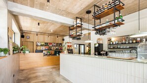 Un espace bar moderne avec un comptoir d’accueil en bois, des étagères remplies de bouteilles et un comptoir recouvert de carreaux.