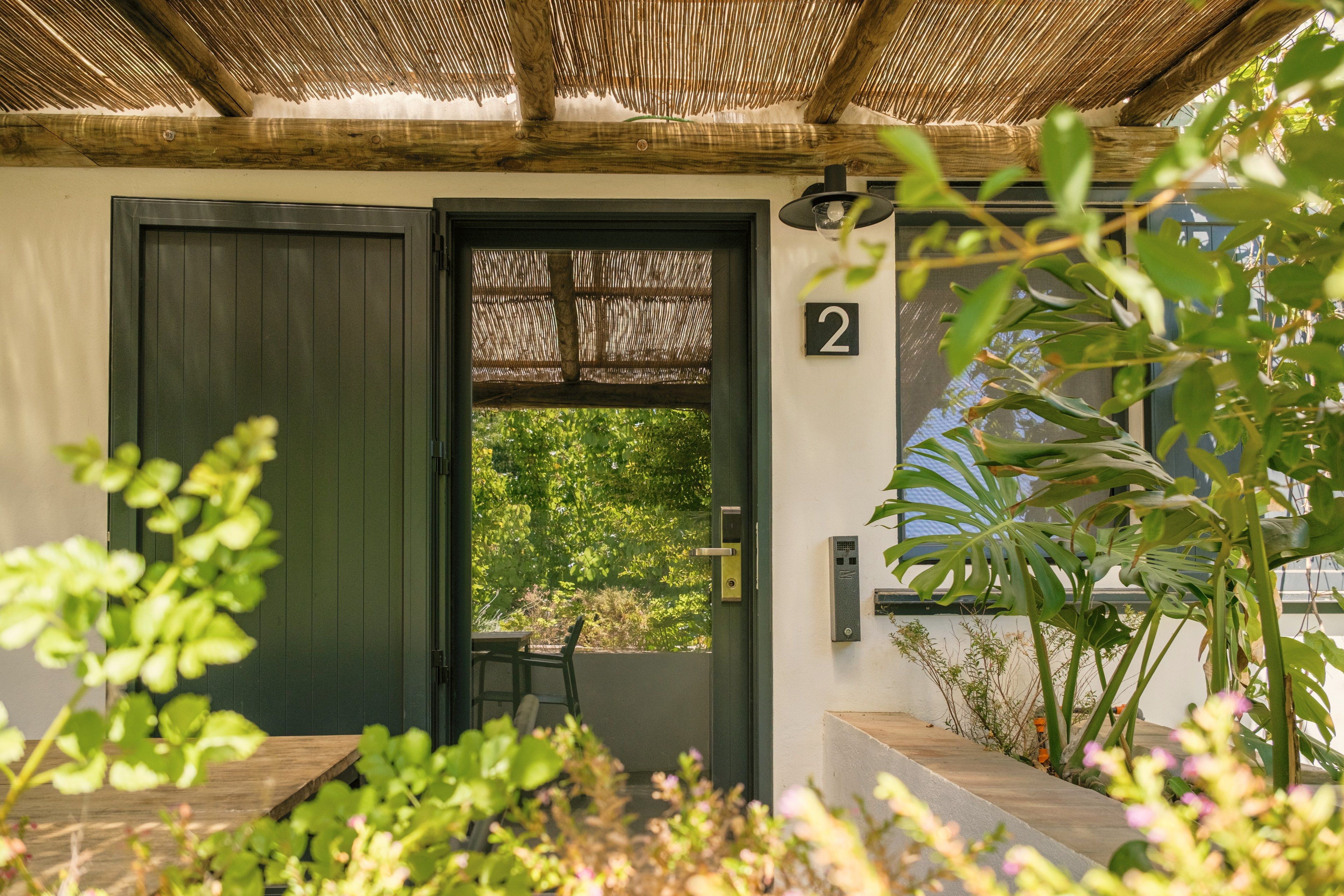 A door with a number '2' sign, a wooden bench, and a view of greenery outside.