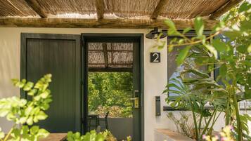A door with a number '2' sign, a wooden bench, and a view of greenery outside.