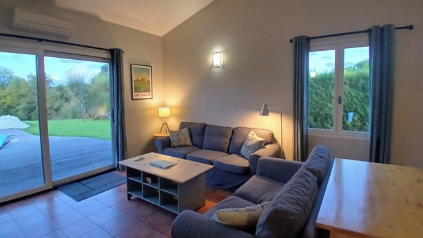 A living room with a sofa, coffee table, and a lamp. There is a window with curtains and a door leading to a balcony. - Spacious villa Le Charme with heated pool, 4 bedrooms sleeping 9, Airco & WiFi (Chalais)