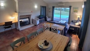 A spacious living area with a fireplace, seating, a dining table, and a large window offering a view of the outdoors. - Spacious villa Le Charme with heated pool, 4 bedrooms sleeping 9, Airco & WiFi (Chalais)