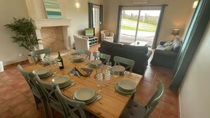 A dining area with a wooden table set for six, surrounded by green chairs. A fireplace is visible in the background, and a sofa is placed in the adjacent living area. - Spacious villa Le Charme with heated pool, 4 bedrooms sleeping 9, Airco & WiFi (Chalais)