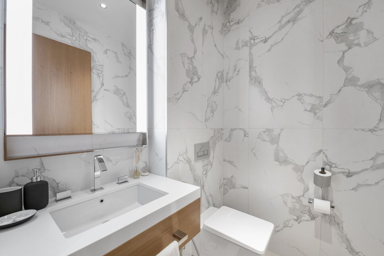 Ein modernes Badezimmer mit Marmorverkleidung, einem großen Spiegel, einem Waschbecken und einer Toilette.