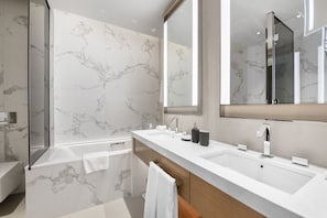 A modern bathroom with marble walls, a large mirror, a bathtub, and a long vanity with multiple sinks. - StoneTree - Luxury 1BR - Prime Location (Dubai)