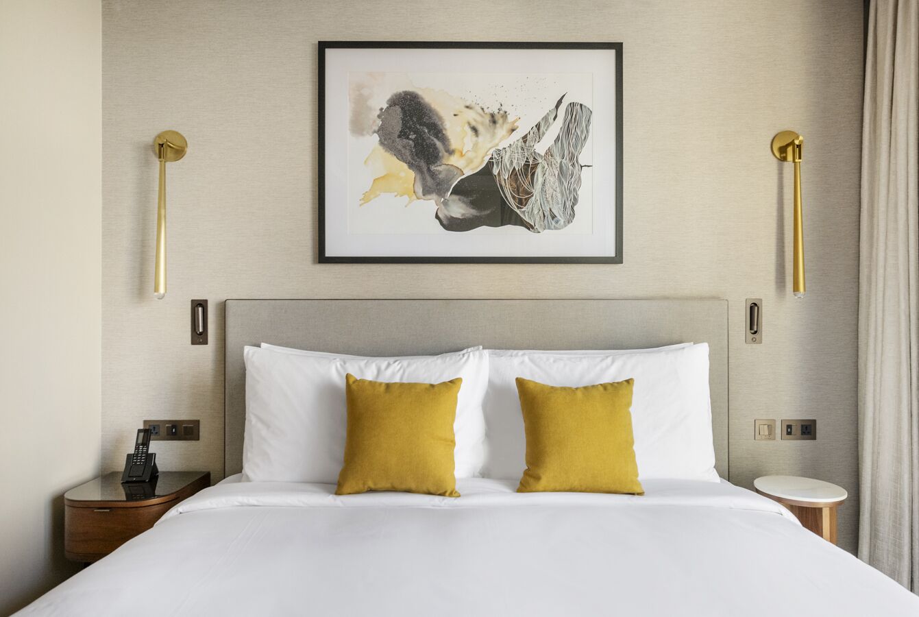 Une chambre d’hôtel avec un grand lit, deux oreillers, une table de chevet avec un téléphone et une œuvre d’art accrochée au mur.