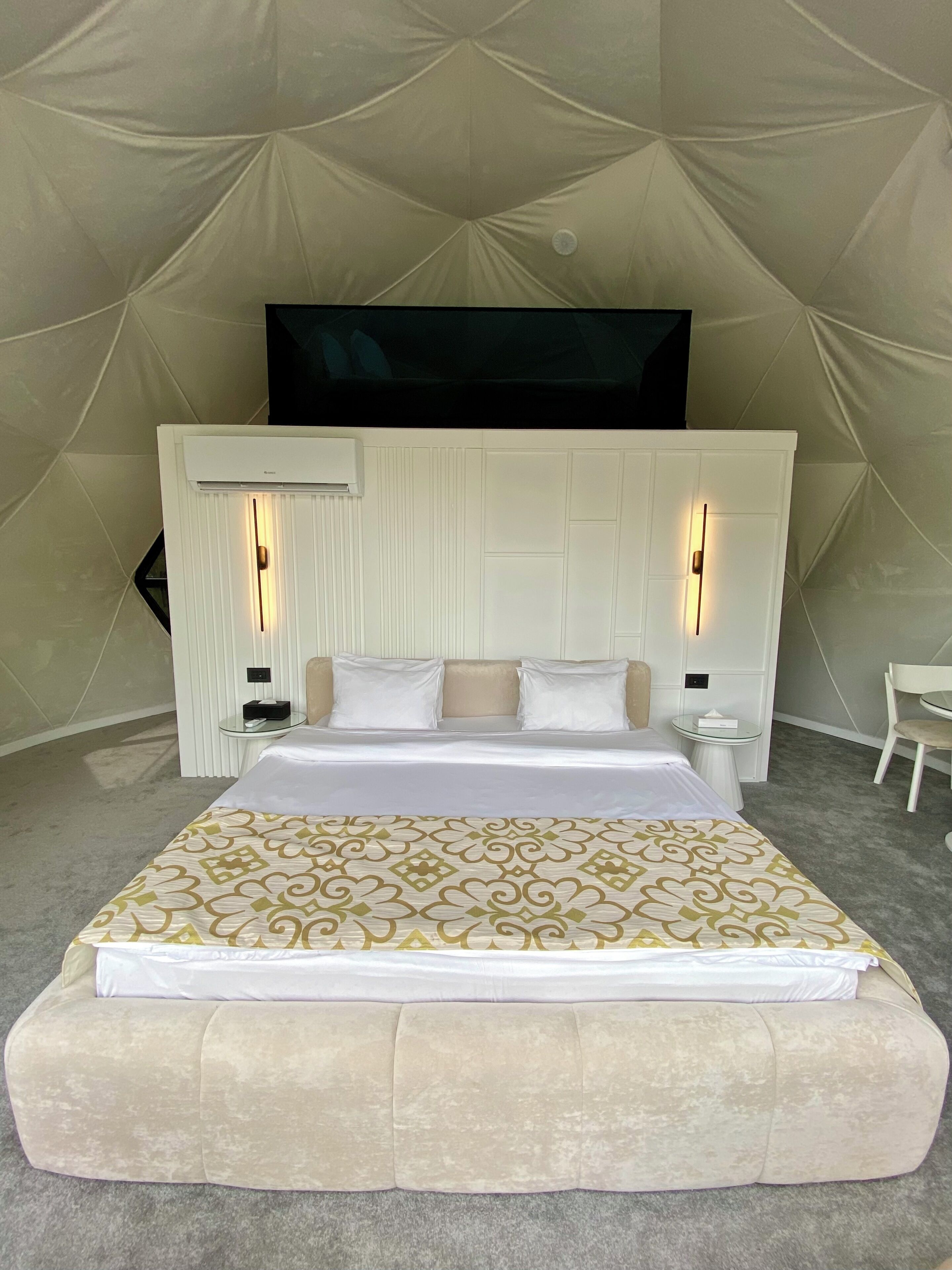A bedroom with a bed, bedside tables, a TV mounted on the wall, and a chair.