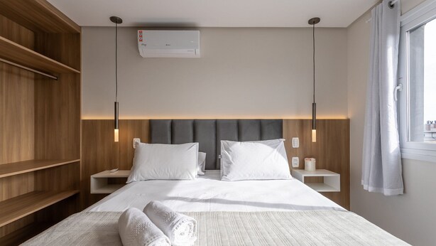 Habitación de hotel con cama, dos mesitas de noche, aire acondicionado de pared y ventana con cortinas.