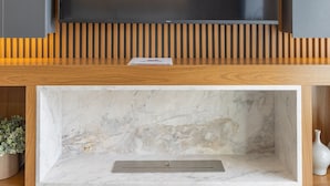 Una sala de estar moderna con un televisor de pantalla plana grande montado en una pared de listones de madera, una chimenea de mármol debajo y una pequeña planta en maceta a la izquierda.