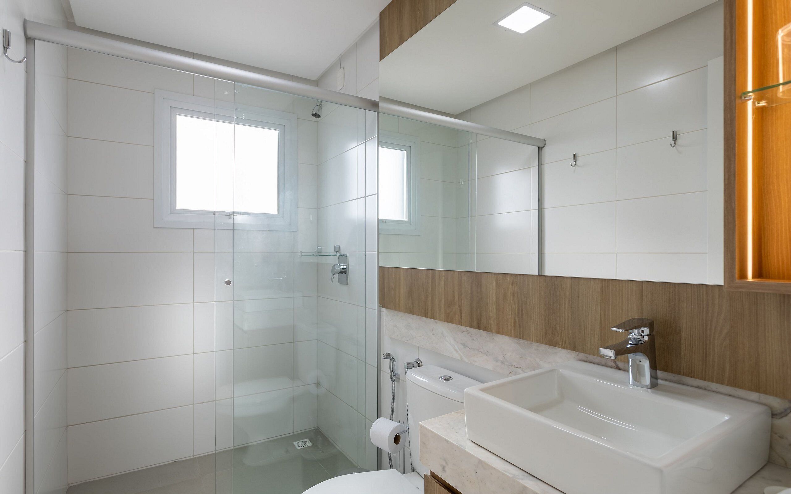 Un bagno moderno con box doccia in vetro, un water, un lavabo con specchio e una parete decorata in legno.