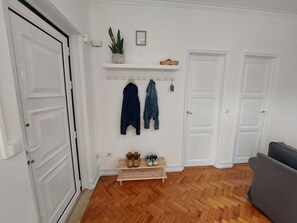 A living room with a wooden herringbone floor, white walls, and a gray sofa. There is a shoe rack with shoes and a potted plant on a shelf. - Luxurious Casa Rio Zêzere River Beaches & Mountains Pets & Kids Welcome (Castelo Branco)