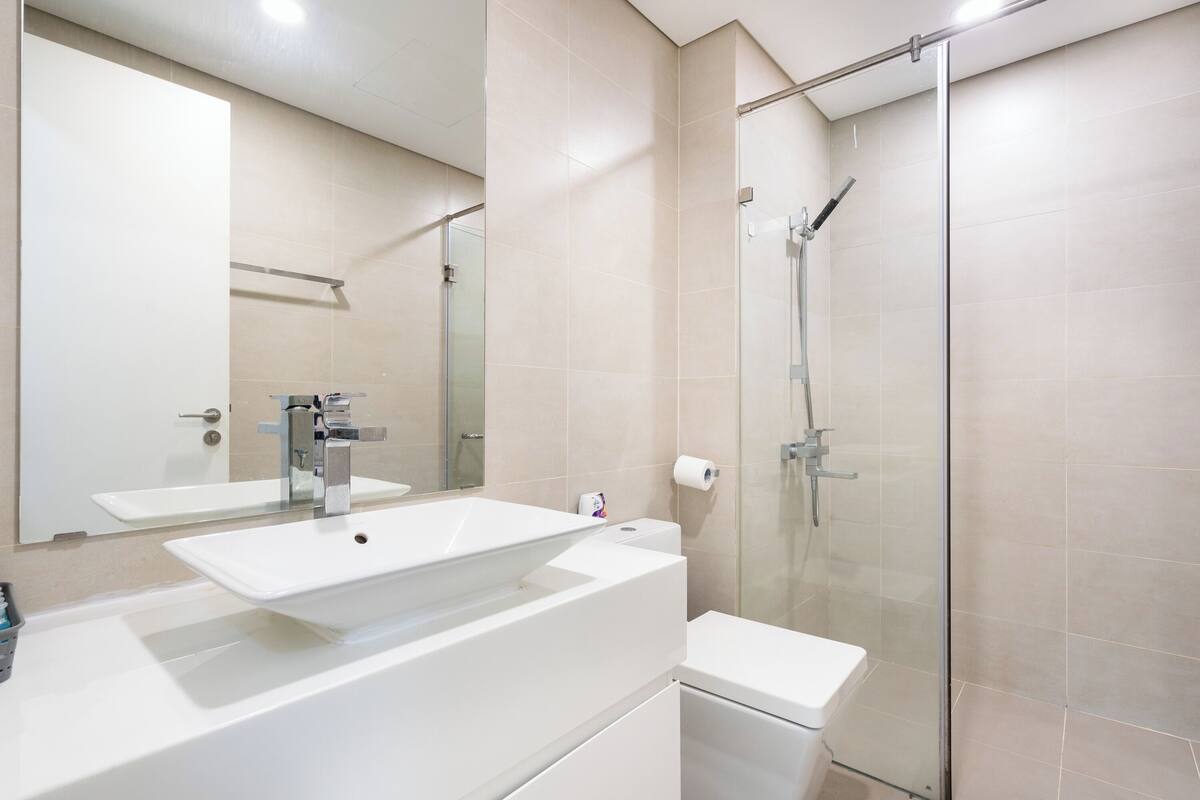 A modern bathroom with a large mirror, a white sink, and a glass-enclosed shower.