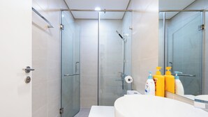 A modern bathroom with a glass-enclosed shower, a white toilet, and a large sink with toiletries. - Hapi Riverside Apartment (Ho Chi Minh City)