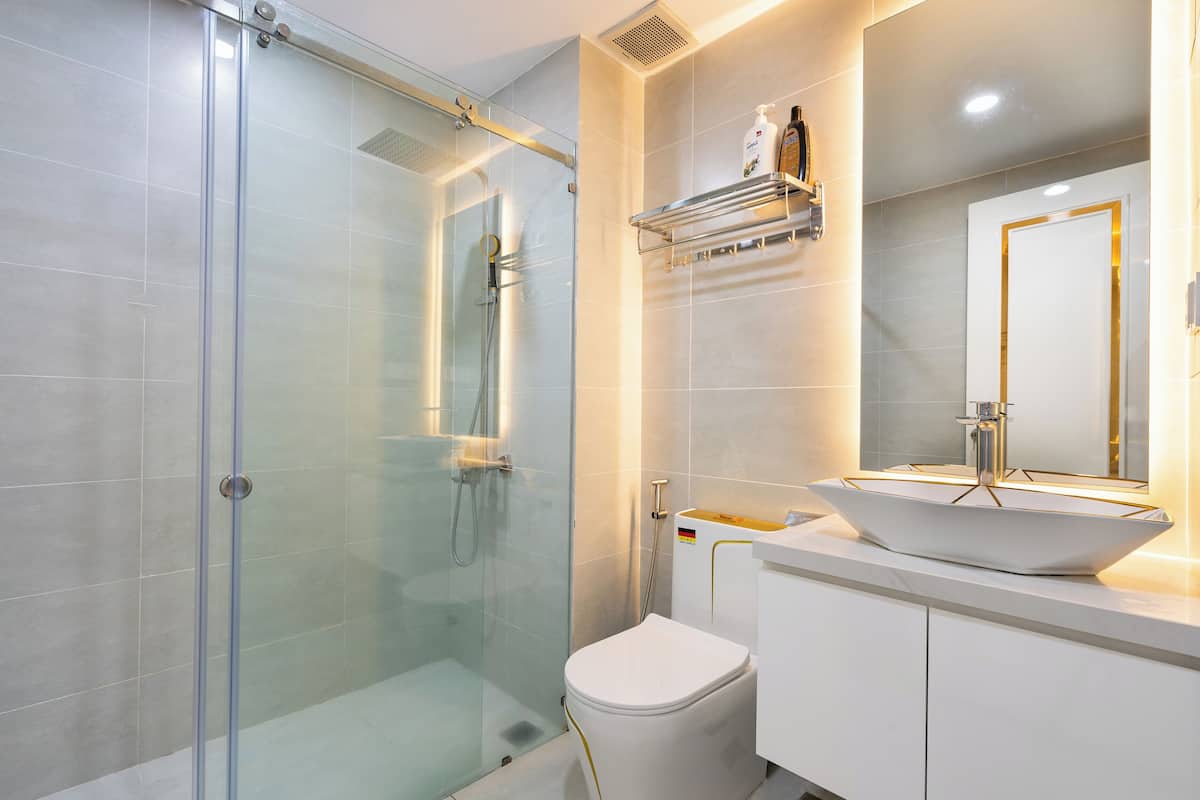 A modern bathroom with a glass-enclosed shower, a white toilet, and a vanity with a large mirror and a vessel sink.