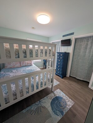 Een slaapkamer met een stapelbed, een dressoir, een televisie en een raam met gordijnen.