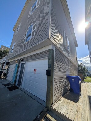 Een woonhuis met twee verdiepingen, een garagepoort, een brievenbus en een blauwe container voor recycling.