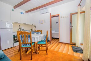 Uma cozinha compacta com uma mesa de jantar e cadeiras, uma pequena geladeira e uma porta deslizante que dá para um quarto.