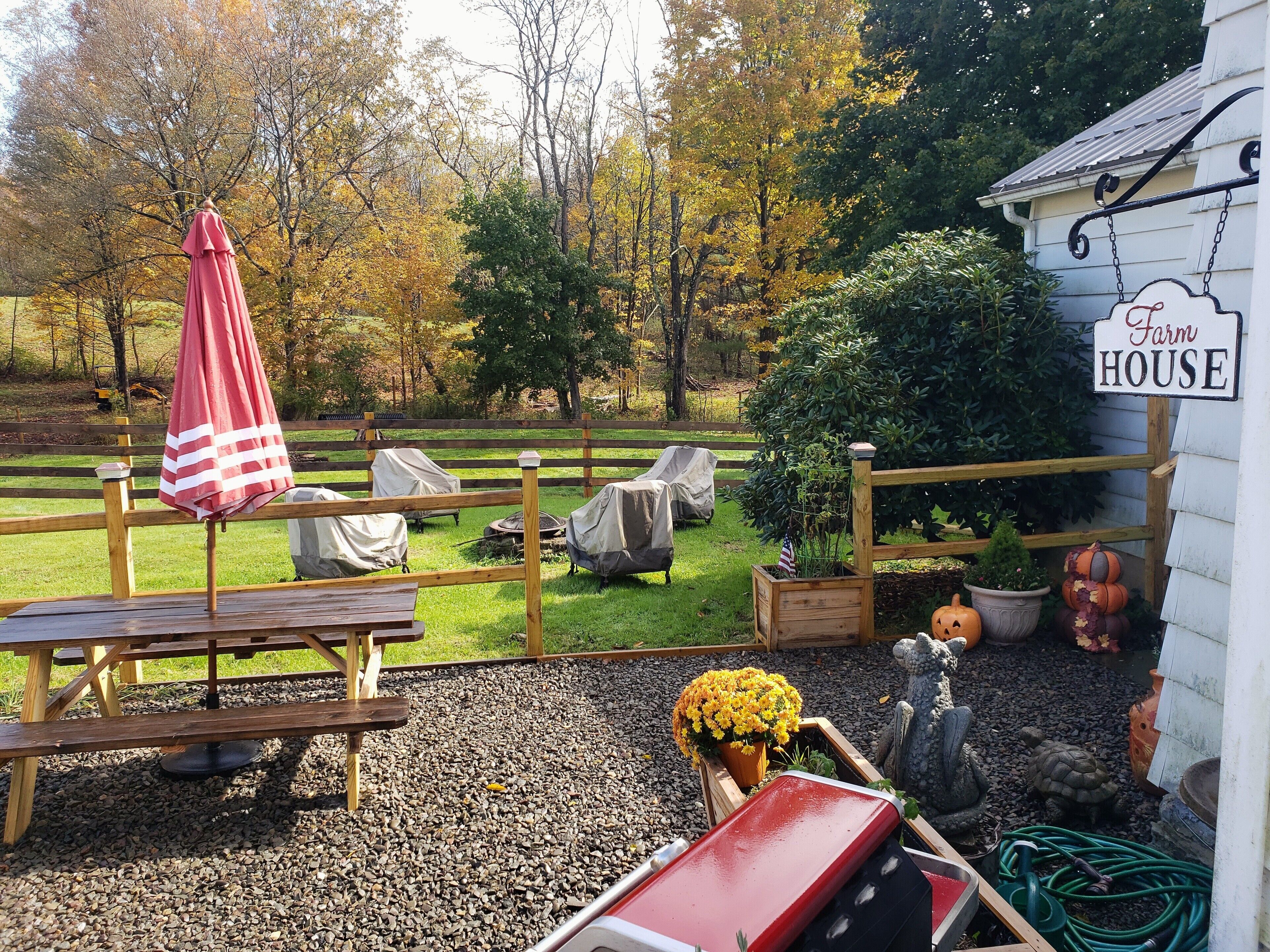 A rustic outdoor seating area with a wooden table and chairs, a covered umbrella, and a sign reading "Farm House."