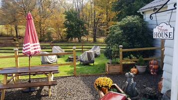 A rustic outdoor seating area with a wooden table and chairs, a covered umbrella, and a sign reading "Farm House."