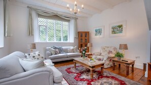 A spacious living room with a sofa, armchairs, a coffee table, and a large window with curtains.