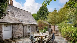 A stone house with a tiled patio, a round wooden table, and six chairs.