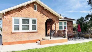 Una casa a un piano in mattoni con un portico coperto, un piccolo garage annesso e un patio con mobili da esterno.