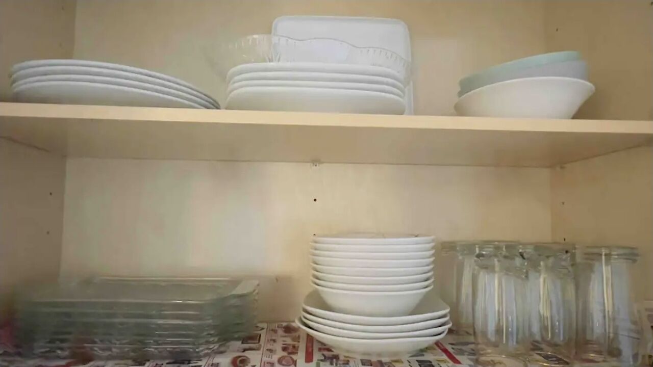 A shelf with stacked white plates and bowls, and a table with clear glass containers.