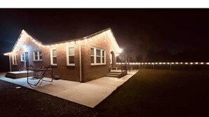 Una casa in mattoni con veranda e piccolo giardino antistante, illuminata da luci decorative.
