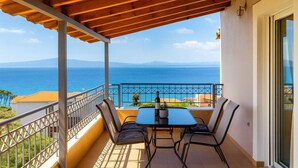 A balcony with a wooden pergola, a table with chairs, and a view of the sea. - Verga Beachside Getaway with Panoramic Seaviews (Paralia Vergas)
