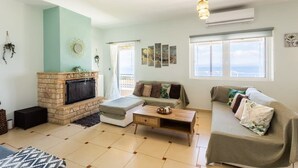 A living room with a fireplace, a sofa, a coffee table, and a large window with a view. - Verga Beachside Getaway with Panoramic Seaviews (Paralia Vergas)