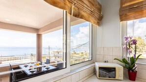 A kitchen with a view of the sea, a microwave, and a dining area with a table and chairs. - Verga Beachside Getaway with Panoramic Seaviews (Paralia Vergas)