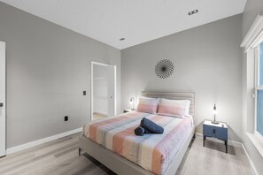 A modern bedroom with a large bed, a bedside table with a lamp, and a decorative wall piece. - 5390 Vacation Sunset House Private Pool Grill (Kissimmee)