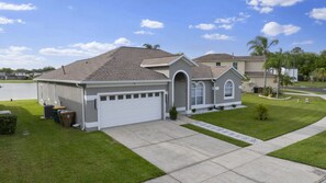 A single-story house with a garage, a small porch, and a well-maintained lawn. - 5390 Vacation Sunset House Private Pool Grill (Kissimmee)