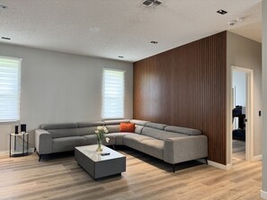 A modern living room with a sectional sofa, a coffee table, and a wooden accent wall. - 5390 Vacation Sunset House Private Pool Grill (Kissimmee)