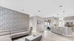 Un salon moderne avec un canapé d’angle gris, une table basse et un coin cuisine doté d’un bar et de tabourets hauts.