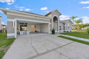A two-story house with a covered garage, a front porch, and a small front yard. - 5390 Vacation Sunset House Private Pool Grill (Kissimmee)