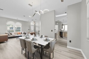 Un espace repas moderne avec une table blanche dressée pour six personnes, entourée de chaises aux couleurs neutres.