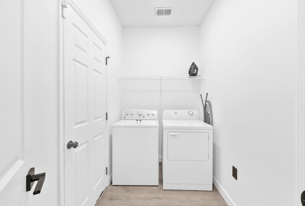 A laundry room with two white washing machines and a dryer, a white door, and a shelf with a few items on it. - 5390 Vacation Sunset House Private Pool Grill (Kissimmee)