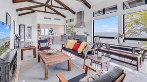 A spacious living area with a wooden ceiling, a sofa with colorful cushions, a coffee table, and a view of the sea through large windows. - The Cape House 6031rpf 2 Bedroom Home by RedAwning (Rockport)