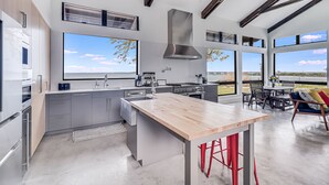 A modern kitchen with a large island, stainless steel appliances, and large windows offering a view of the outdoors. - The Cape House 6031rpf 2 Bedroom Home by RedAwning (Rockport)