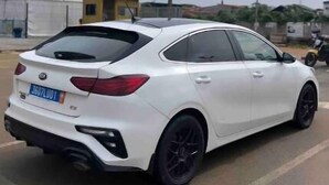 Un auto blanco estacionado en un estacionamiento, con una carpa blanca y un edificio amarillo al fondo.