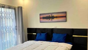Un dormitorio con cama, cabecera, obra de arte en la pared y ventana con cortinas.