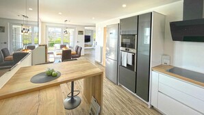 Une cuisine moderne avec une table à manger en bois, un four encastré et un grand réfrigérateur.