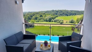 Un balcon agrémenté de meubles en osier, une petite table avec des boissons, et une vue sur une piscine et un paysage verdoyant.