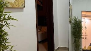 A hallway with a geometric painting on the wall, a door leading to a room, and a potted plant. - La Liga, 2 Bedrooms (Abidjan)