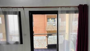 A living room with a sofa, a red chair, and a view of a balcony with a green lawn. - La Liga, 2 Bedrooms (Abidjan)