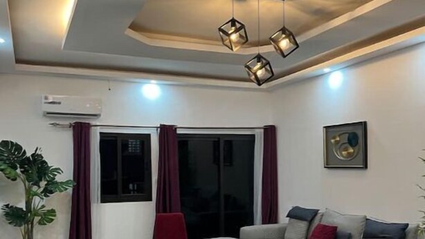 A modern living room with a sectional sofa, a glass coffee table, a red chair, and a potted plant. - La Liga, 2 Bedrooms (Abidjan)